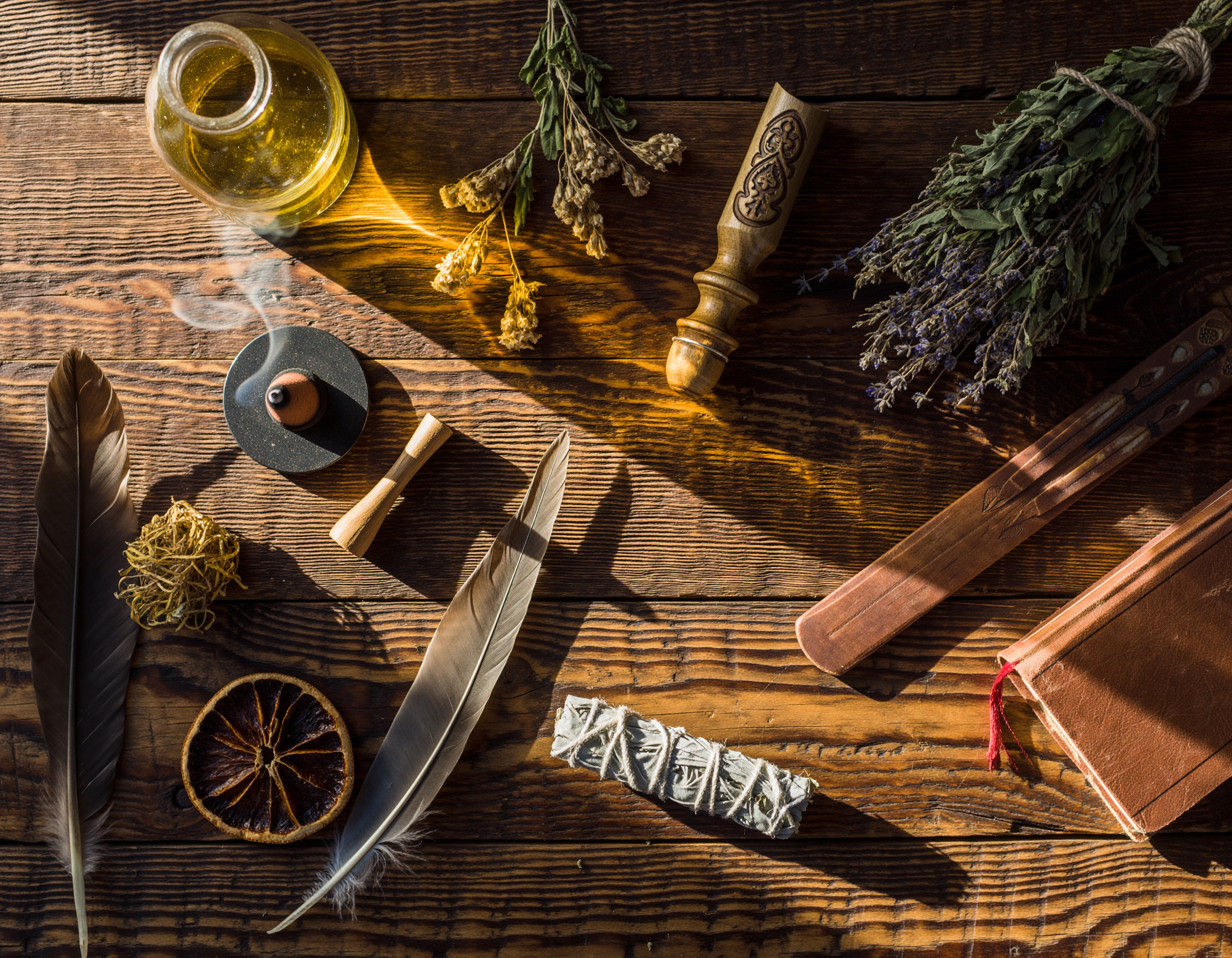 Räucherwerk, getrocknete Kräuter, Federn und spirituelle Utensilien auf einem Holztisch.