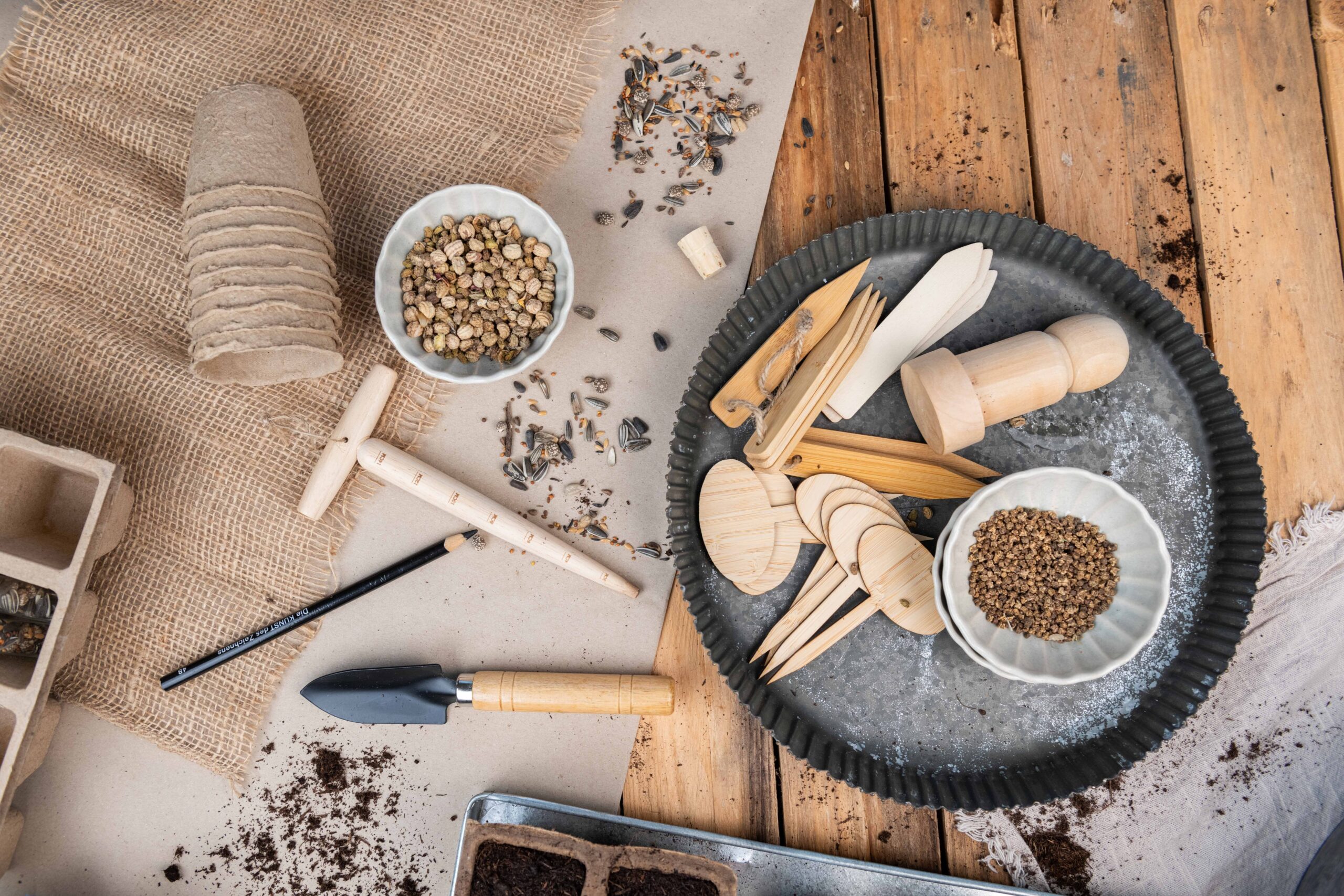 Gartenwerkzeuge, Anzuchttöpfe, Saatgut und Erde auf einem rustikalen Arbeitstisch zur Aussaatvorbereitung.