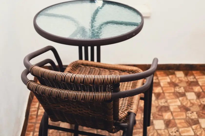 Kleiner Balkontisch mit Stuhl aus Rattan auf gefliestem Balkon.