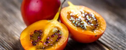 Aufgeschnittene Tamarillo mit gelbem Fruchtfleisch und dunklen Samen auf Holztisch.