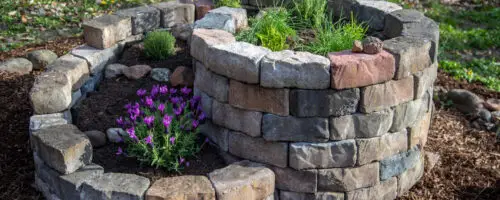 Kräuterschnecke aus Natursteinen mit Kräutern und blühender Pflanze.