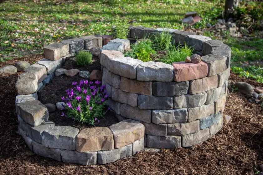 Kräuterschnecke aus Natursteinen mit Kräutern und blühender Pflanze.