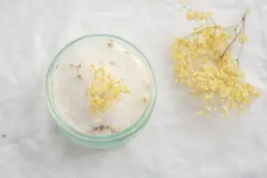 Glas mit Holunderblütenzucker und frischen Holunderblüten auf hellem Hintergrund.