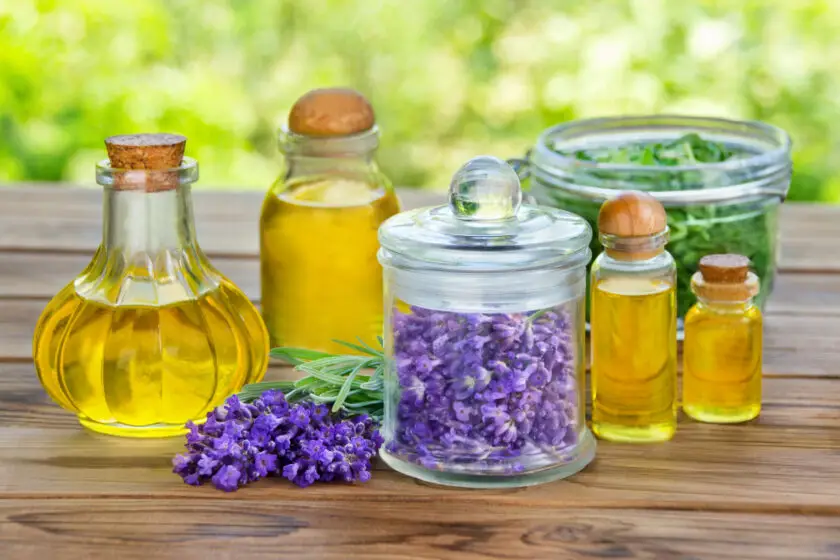 Glasflaschen mit Kräuteröl und Lavendelblüten auf Holztisch im Garten.